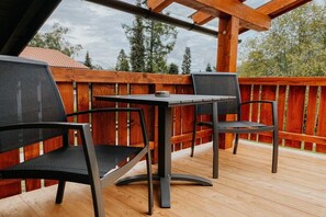 An outdoor deck with a table and two chairs, surrounded by a wooden fence and trees in the background. - Holiday apartment with 1 bedroom (Schönau am Königssee)