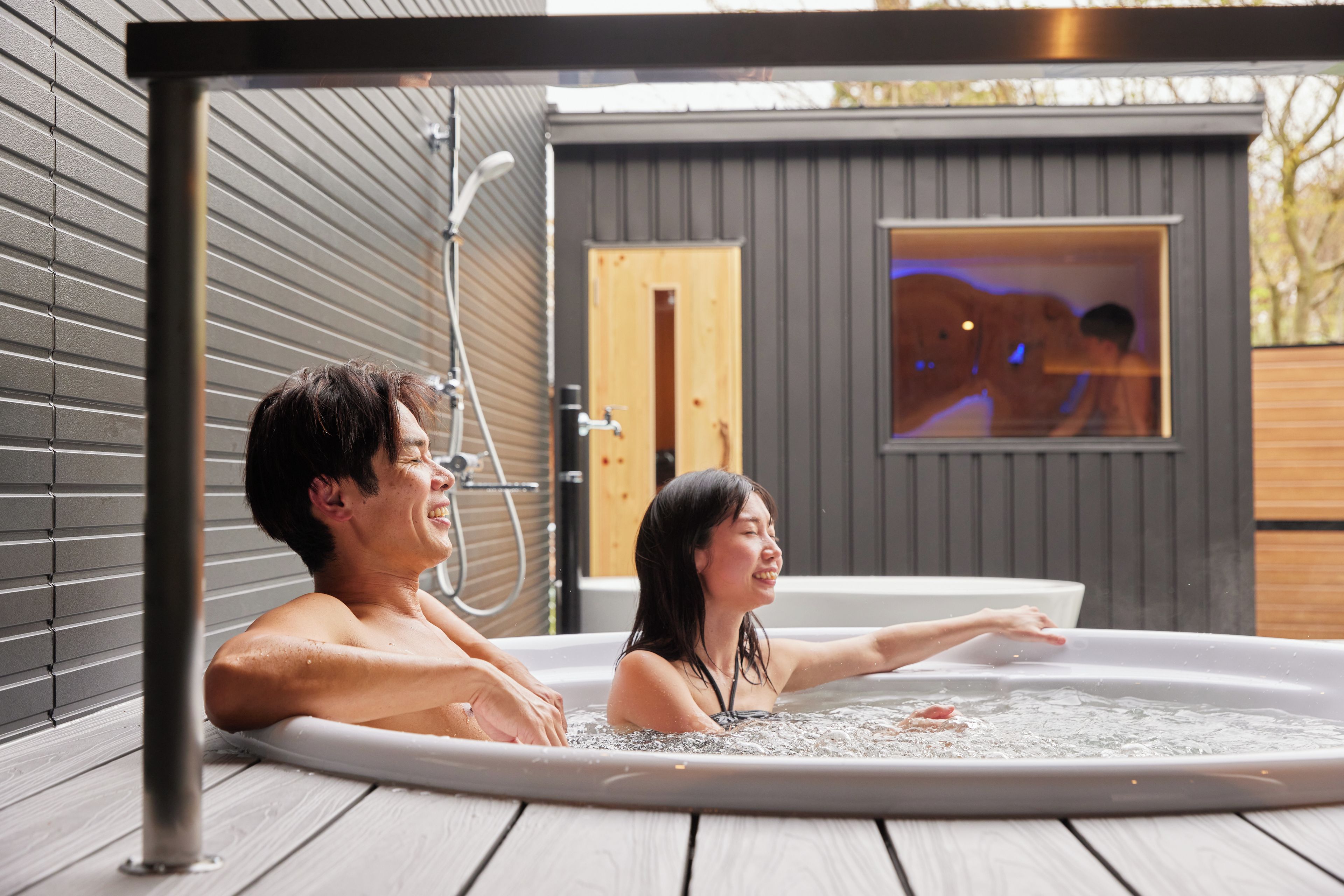 Ein Paar in einer Hot Tub auf einer Holzterrasse, mit Blick auf eine Sauna.