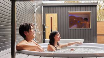 Ein Paar in einer Hot Tub auf einer Holzterrasse, mit Blick auf eine Sauna.