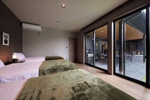 Habitación de hotel con dos camas, un amplio ventanal corredero que da a un área exterior y un equipo de aire acondicionado instalado en el techo.