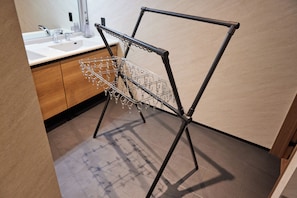 A metal drying rack with clothes hanging in a modern bathroom with wooden cabinets and a white sink.