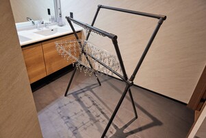Un tendedero metálico con ropa colgada en un baño moderno con armarios de madera y un lavamanos blanco.