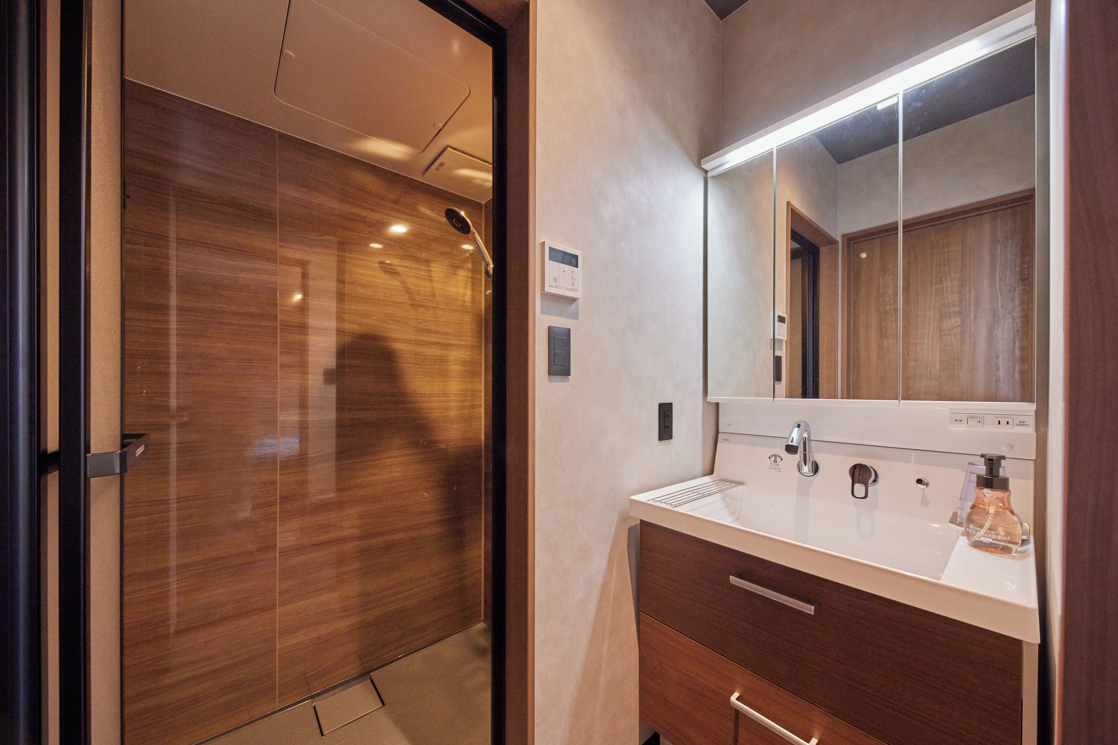 A modern bathroom with a wooden door, a white sink with a mirror, and a bottle of soap.