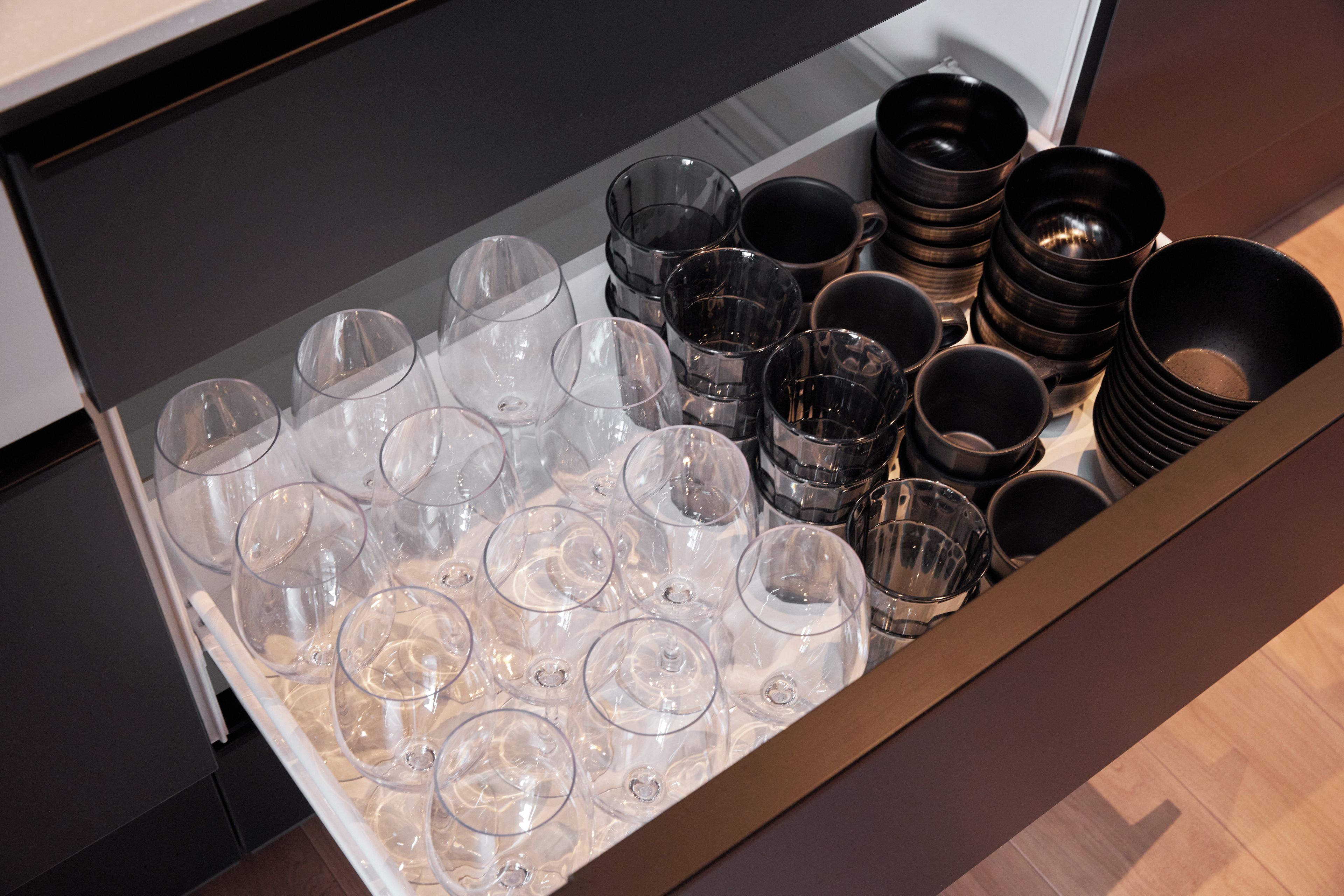 A drawer containing multiple clear wine glasses and black bowls.