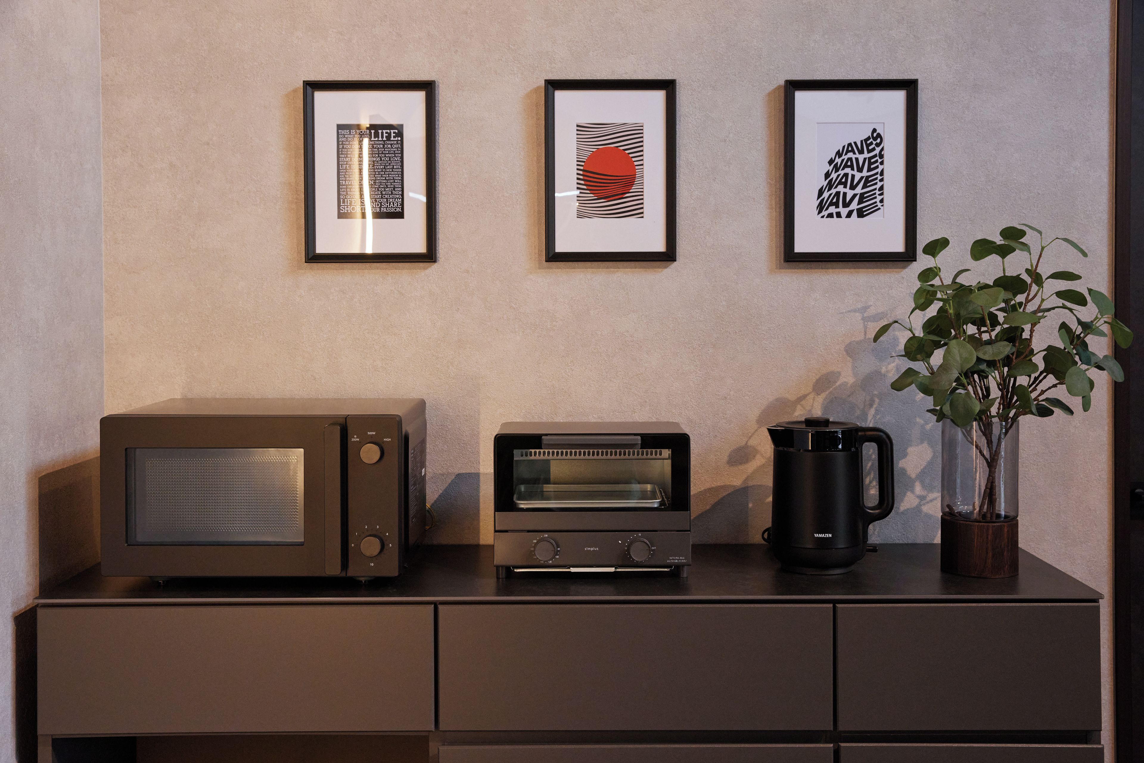 A kitchenette with a microwave, toaster, and coffee maker on a dark countertop.