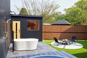 Ein modernes Badezimmer im Freien mit einer freistehenden Badewanne, einer Holztür und einem Fenster.