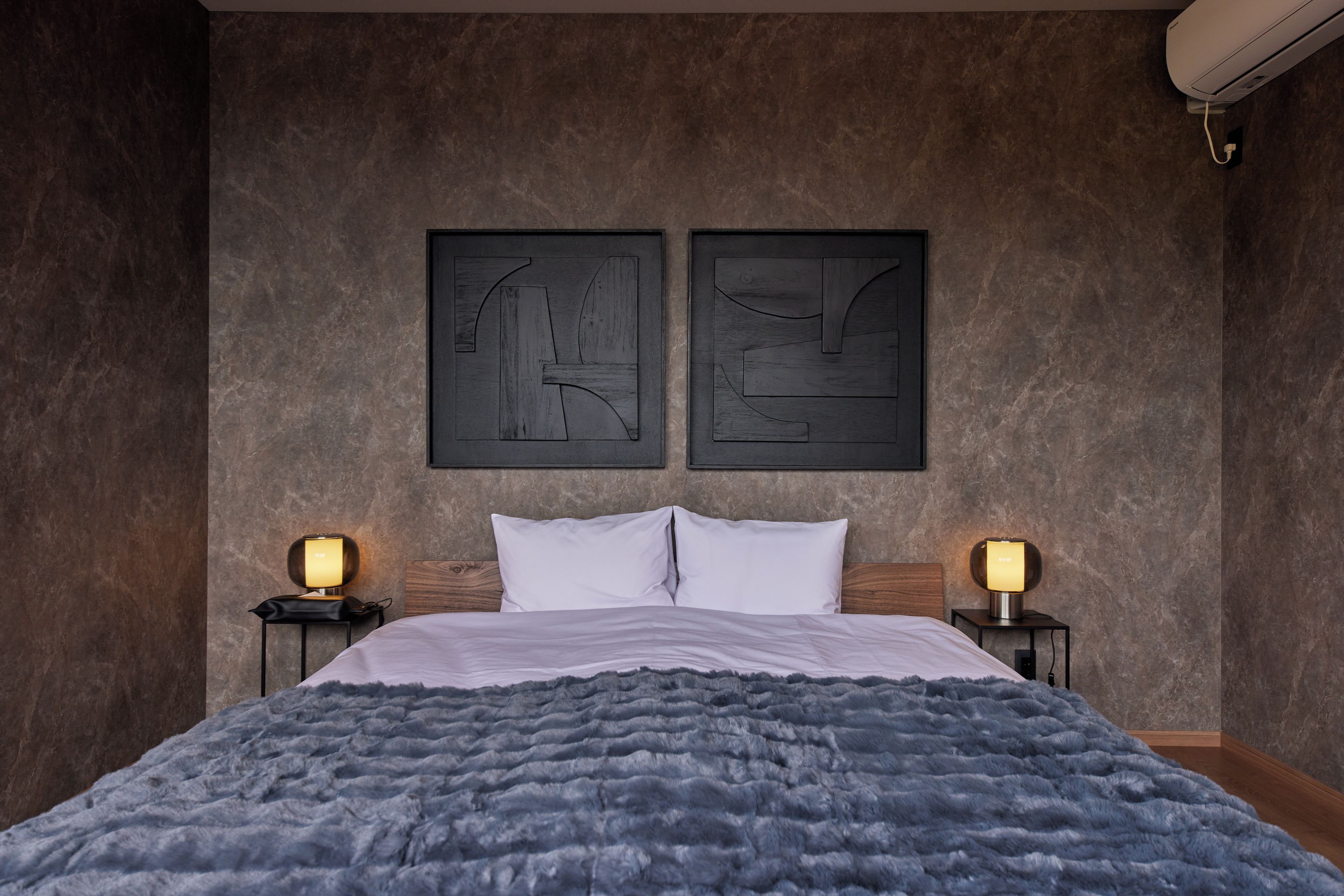 A bedroom with a large bed, two bedside tables with lamps, and abstract wall art.