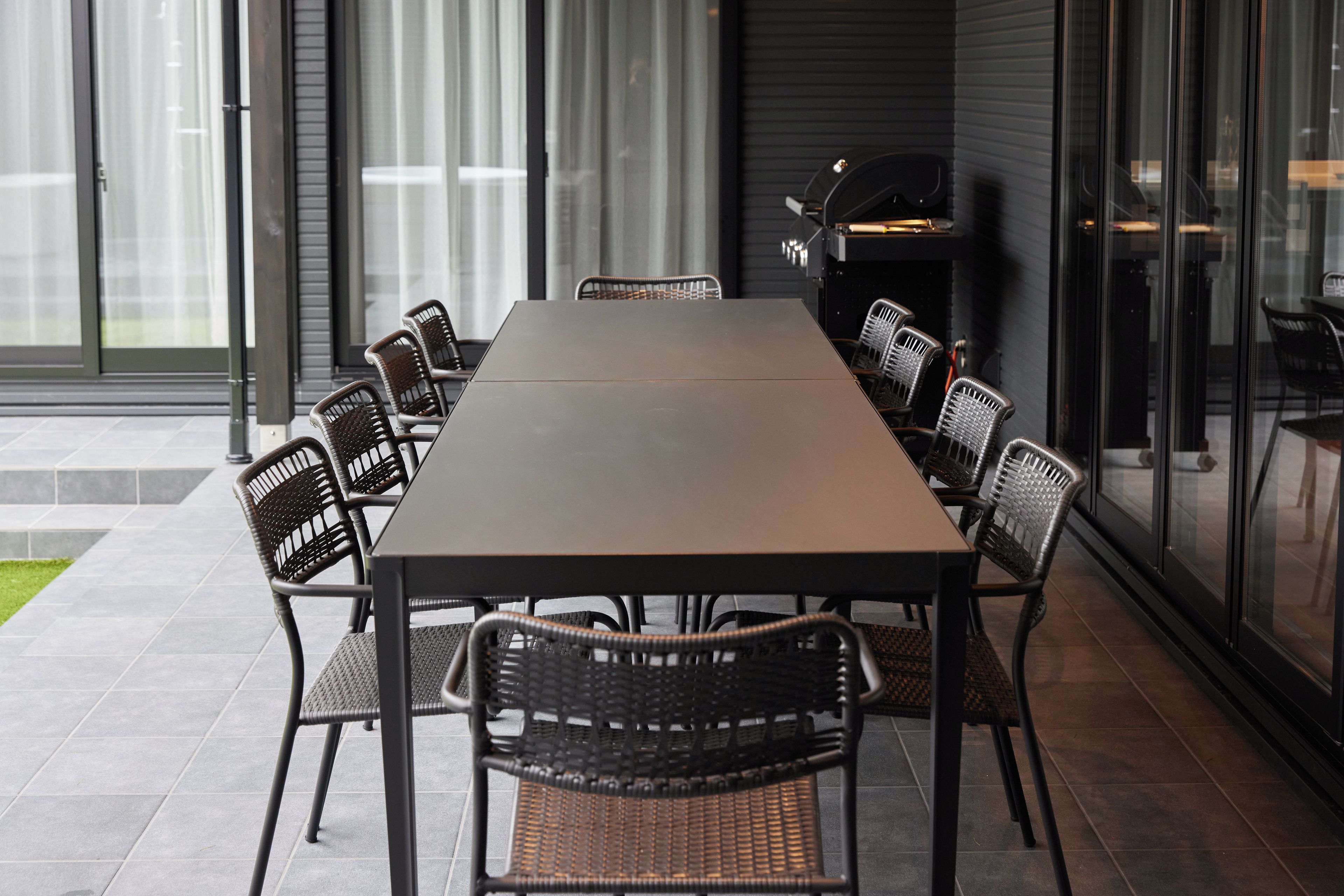 A long dining table with chairs, a grill, and a glass partition.
