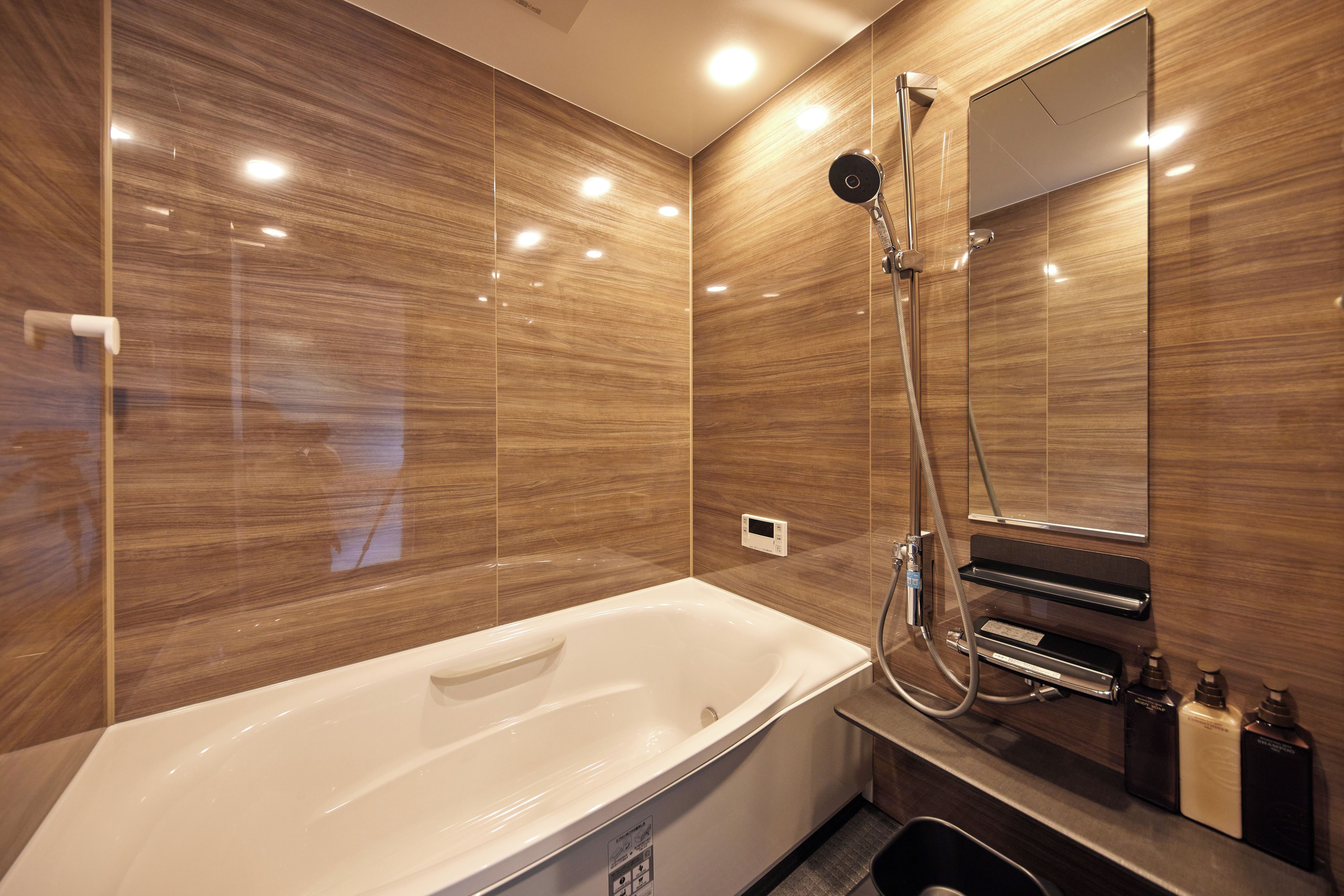 A modern bathroom with a large bathtub, a handheld showerhead, and a built-in mirror.