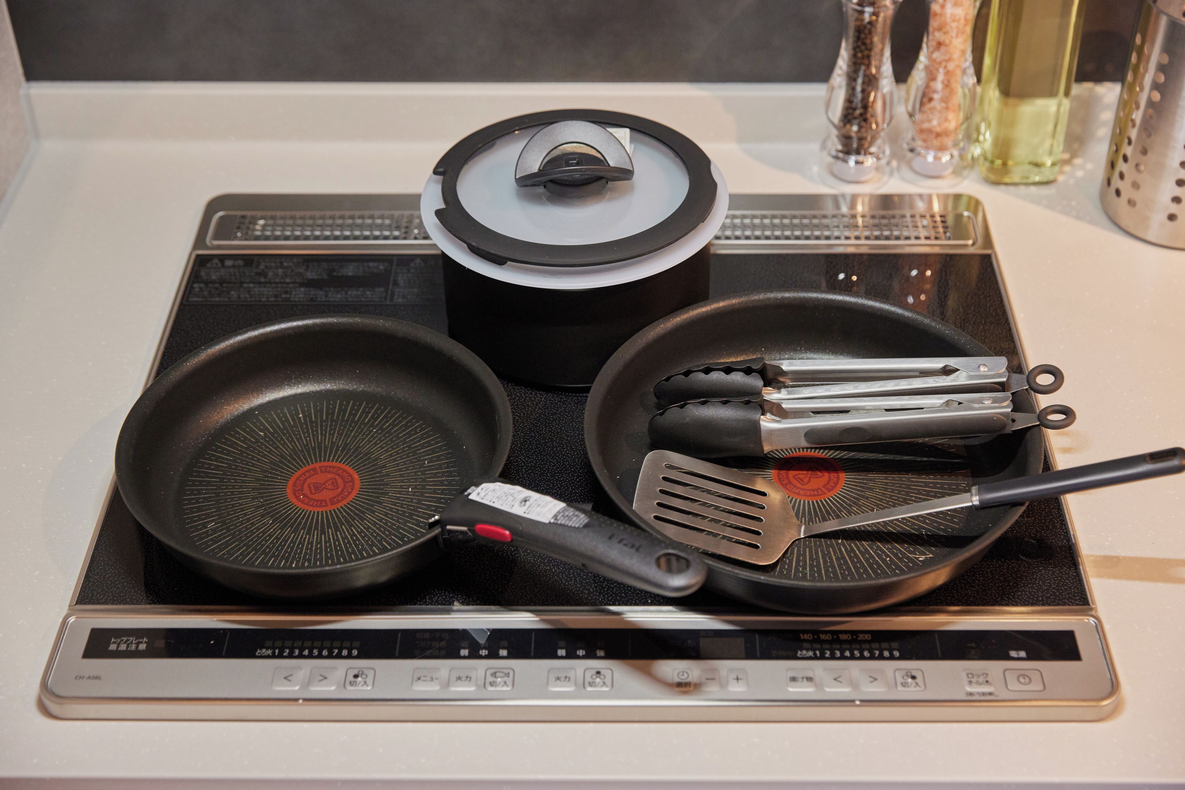 A kitchen with a stove, two frying pans, a pot, and a spatula.