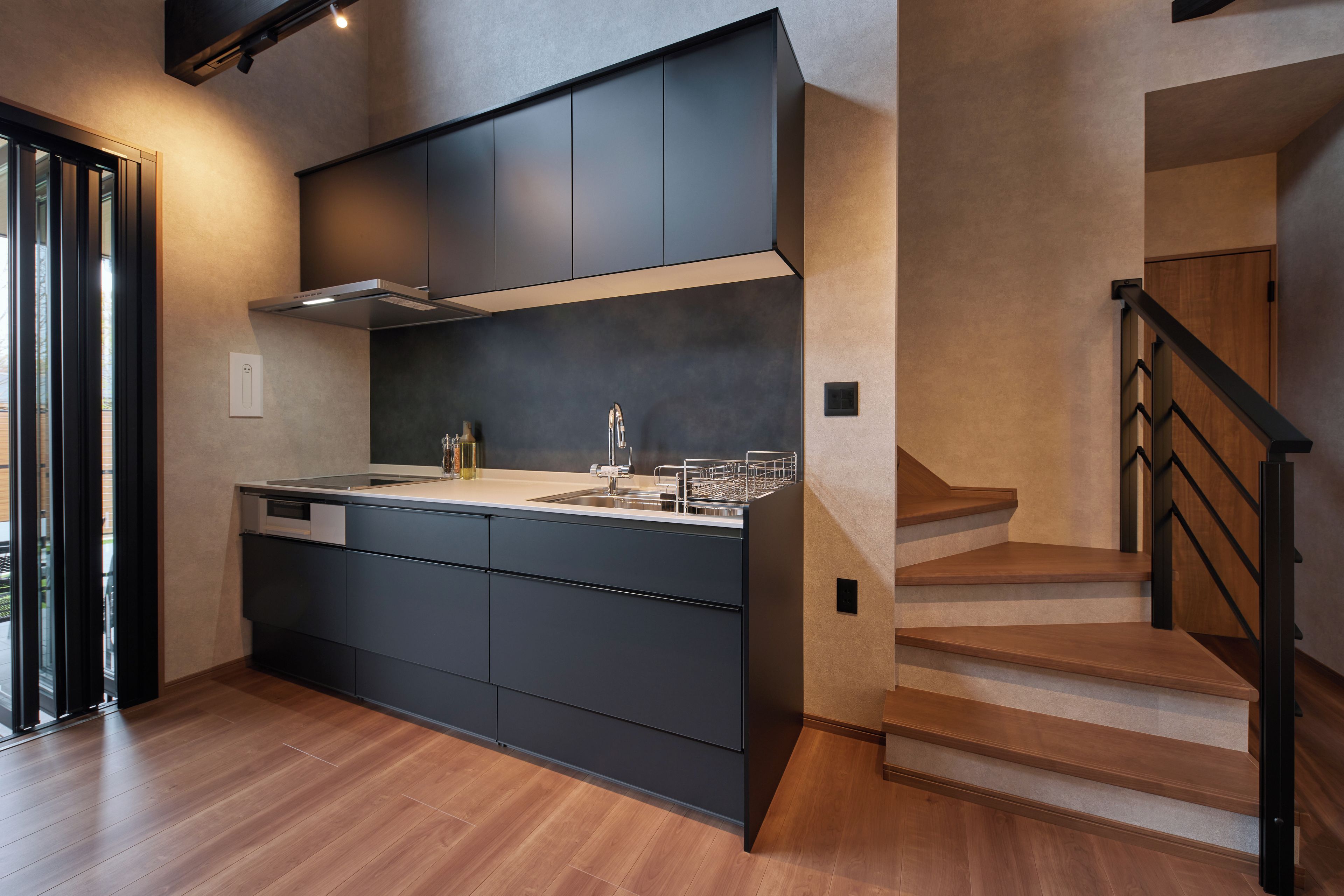 A modern kitchen with a built-in island, stainless steel appliances, and a wooden staircase.