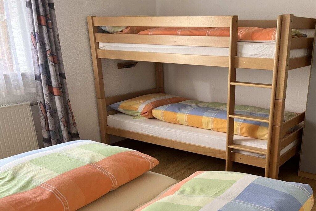 A bunk bed with two levels, a window with curtains, and a radiator.