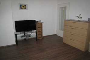 Une pièce avec un téléviseur posé sur un meuble en verre, une commode en bois et une porte agrémentée d’un petit élément décoratif.