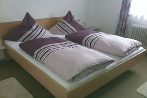Ein Einzelbett mit Holzrahmen, zwei Kissen und einer weißen Matratzenauflage.