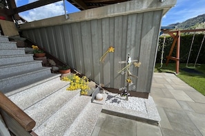 Eine Holzterrasse mit einer Steintreppe zu einem überdachten Bereich, umgeben von einem Holzzaun und einem Garten.