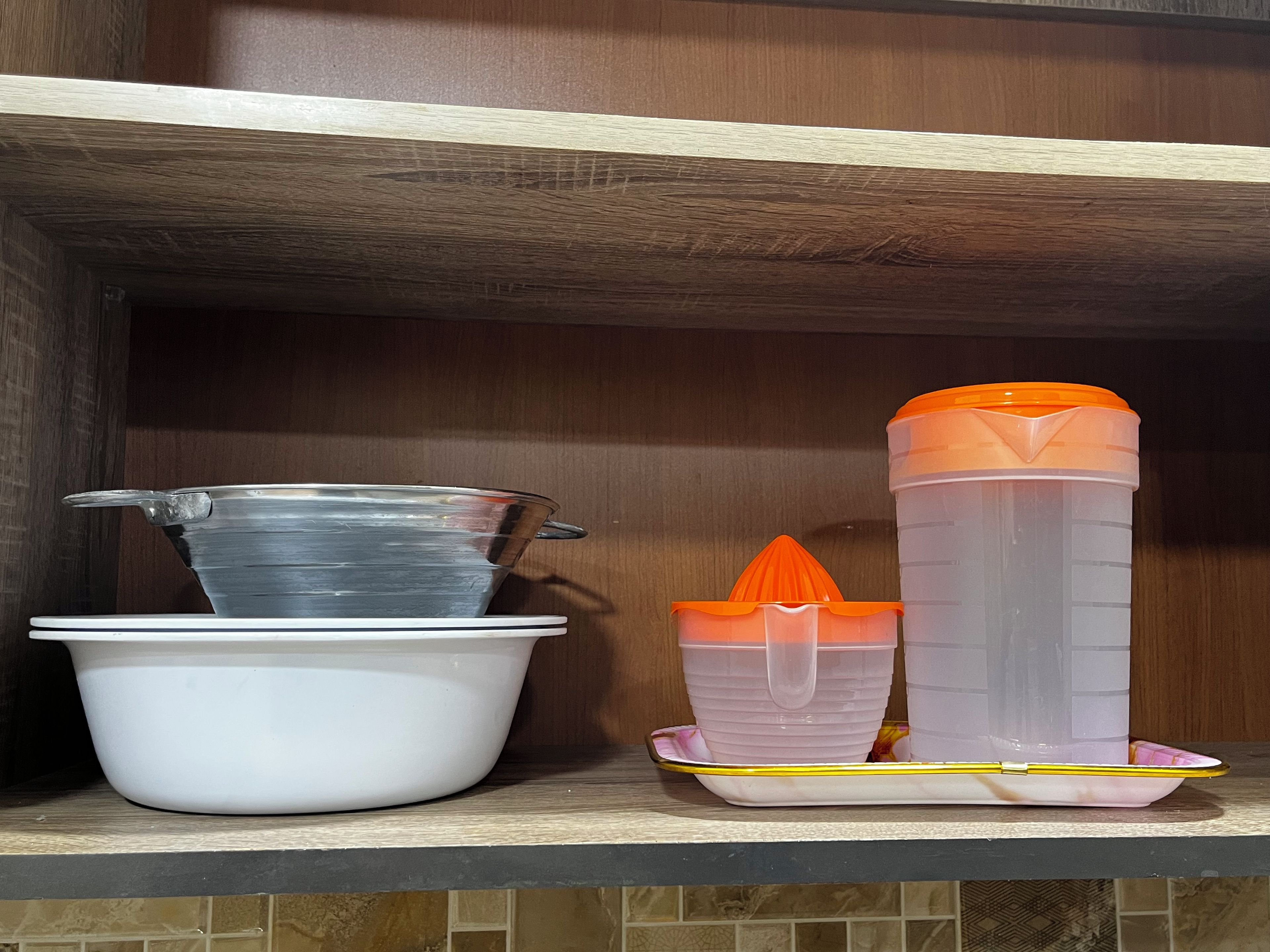 Una repisa de cocina con un tazón blanco, un colador metálico y dos recipientes con tapa naranja.