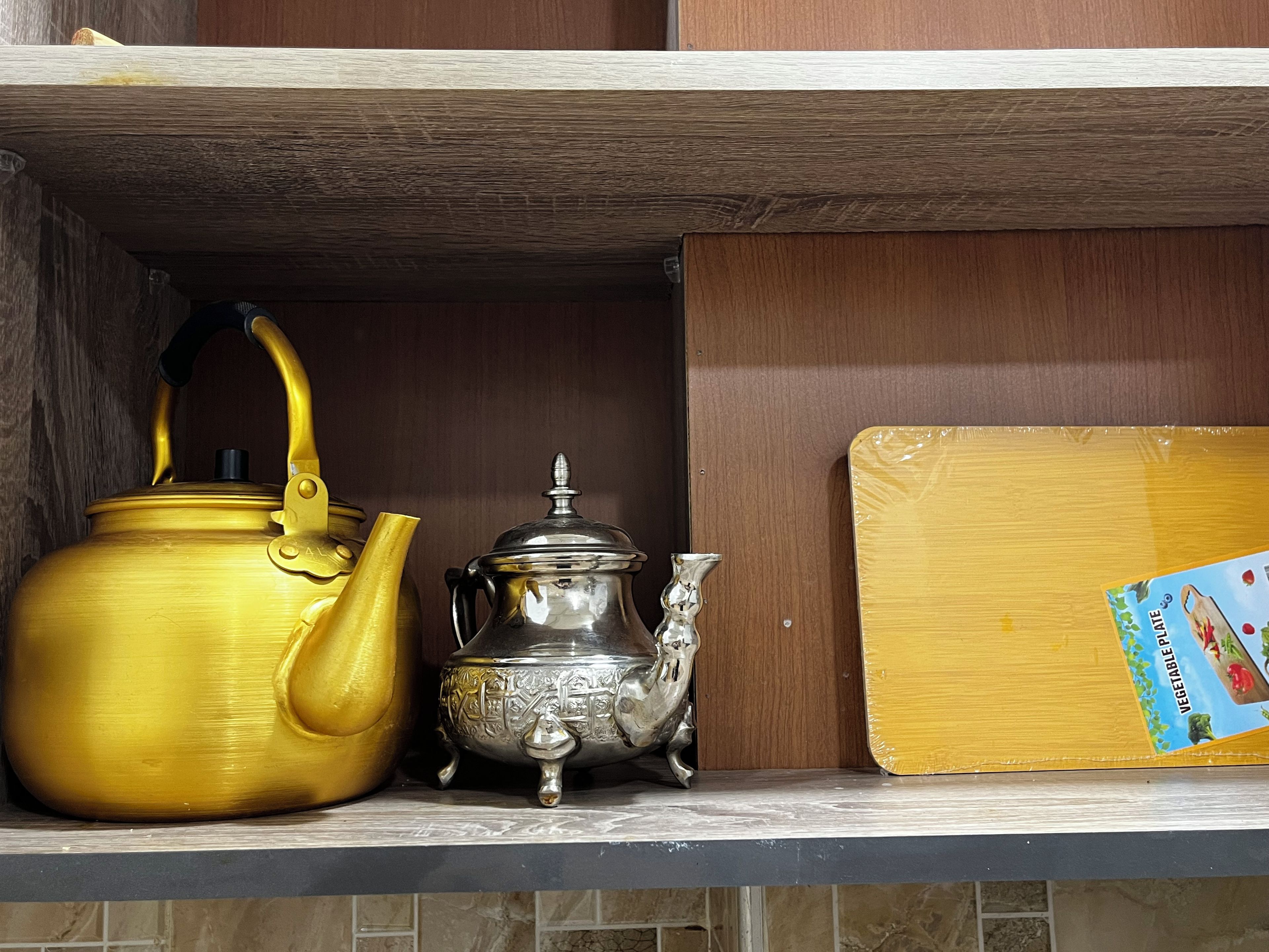 Een plank met een gouden waterkoker, een zilveren theepot en een kartonnen doos met een etiket.