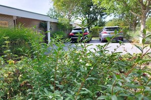 Una entrada de vehículos residencial con dos coches estacionados, rodeada de follaje y un edificio de ladrillo.