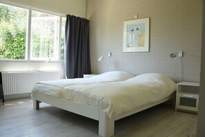 Ein Schlafzimmer mit einem Bett, einem Nachttisch, einem Tisch neben dem Bett, einem Fenster mit Vorhängen, einer Heizung und einem Wandbild.