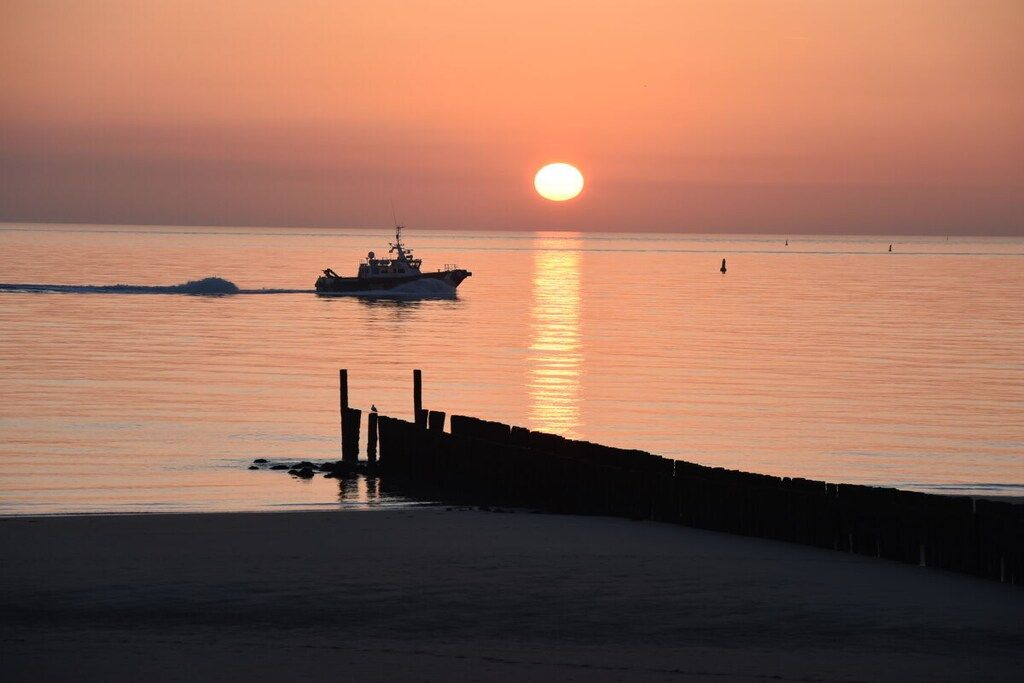 Een zonsondergang boven een rustige zee, met een boot en een steiger.