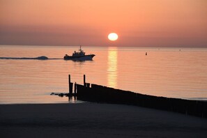 A sunset over a calm sea with a boat and a pier. - Holiday home with 4 bedrooms (Westkapelle)