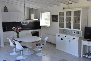 A modern kitchen with white cabinetry, a round dining table with chairs, a hanging light fixture, and a television on a stand. - Holiday home with 4 bedrooms (Westkapelle)