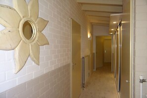 Un pasillo con pared de ladrillo blanco, un espejo grande con forma de flor y puertas que dan a otras habitaciones.