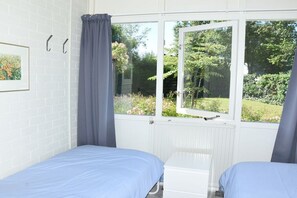 Una habitación con dos camas, una ventana con cortinas, un radiador y un cuadro en la pared.