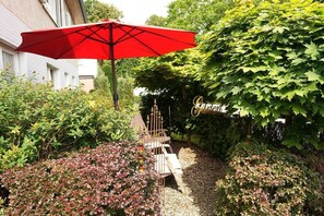 A garden with a red umbrella, a wooden bench, and a sign that reads 'Café'. - Holiday Lounge & Art (Bad Driburg)
