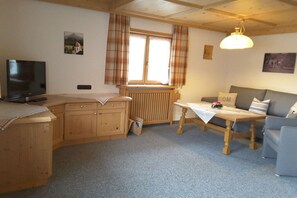 A cozy room with a wooden desk, a television, a sofa, and a window with curtains. - Holiday apartment with 2 bedrooms (Fischen-Au)