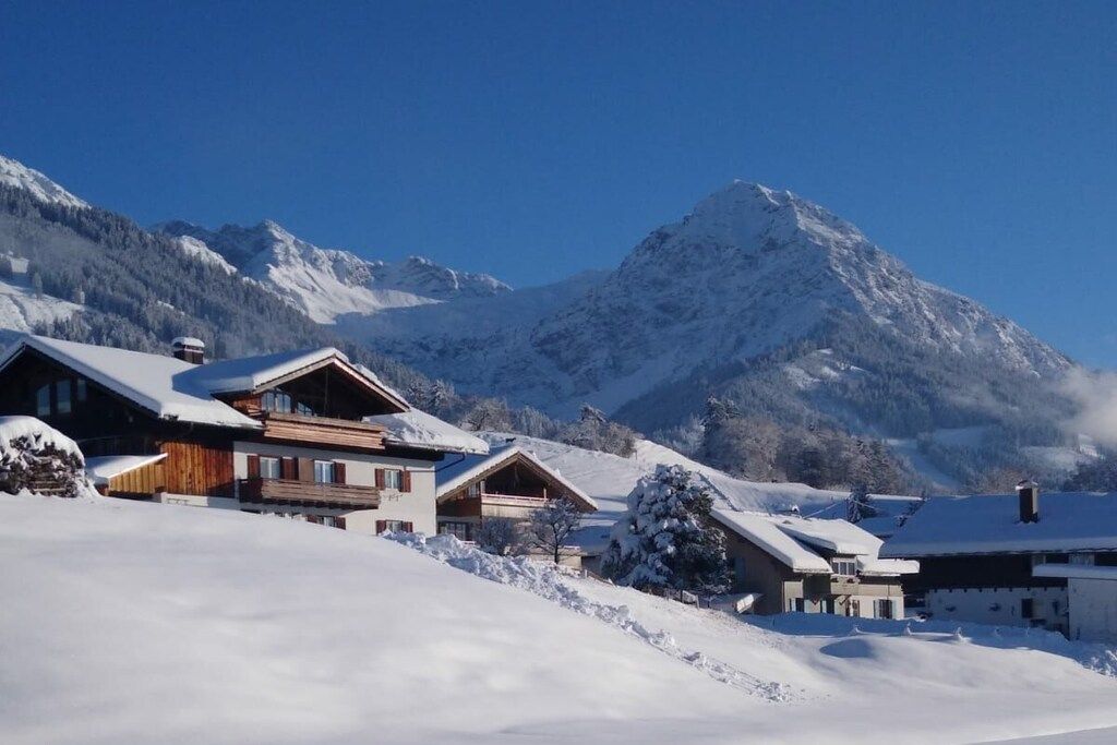 Ein verschneites Bergdorf mit Chalets und einem markanten Berg im Hintergrund.