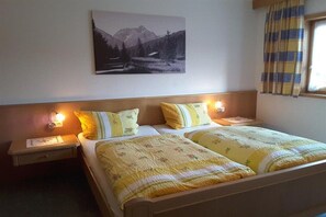 A double bed with two nightstands, each with a lamp, in a room with a mountain landscape painting on the wall. - Holiday apartment with 2 bedrooms (Fischen-Au)