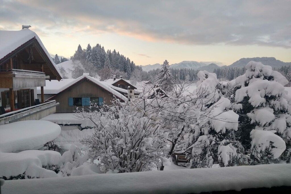 Un village enneigé, avec des bâtiments en bois et une chaîne de montagnes en arrière-plan.
