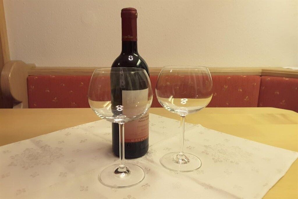 Une bouteille de vin et deux verres sur une table recouverte d’une nappe à motifs floraux.