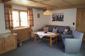 Een gezellige kamer met een bank, een klein tafeltje, een radiator en een raam met gordijnen.