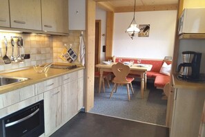 Een kleine keuken met houten kastjes, een inbouwoven en een eethoek met een rode bank en houten stoelen.