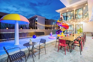 Un espace extérieur aménagé en terrasse, avec une table à manger, des chaises et un élément décoratif aquatique aux couleurs vives.