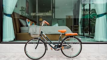 Una bicicleta estacionada frente a un dormitorio moderno con un ventanal grande, una cama y un baño a la vista.