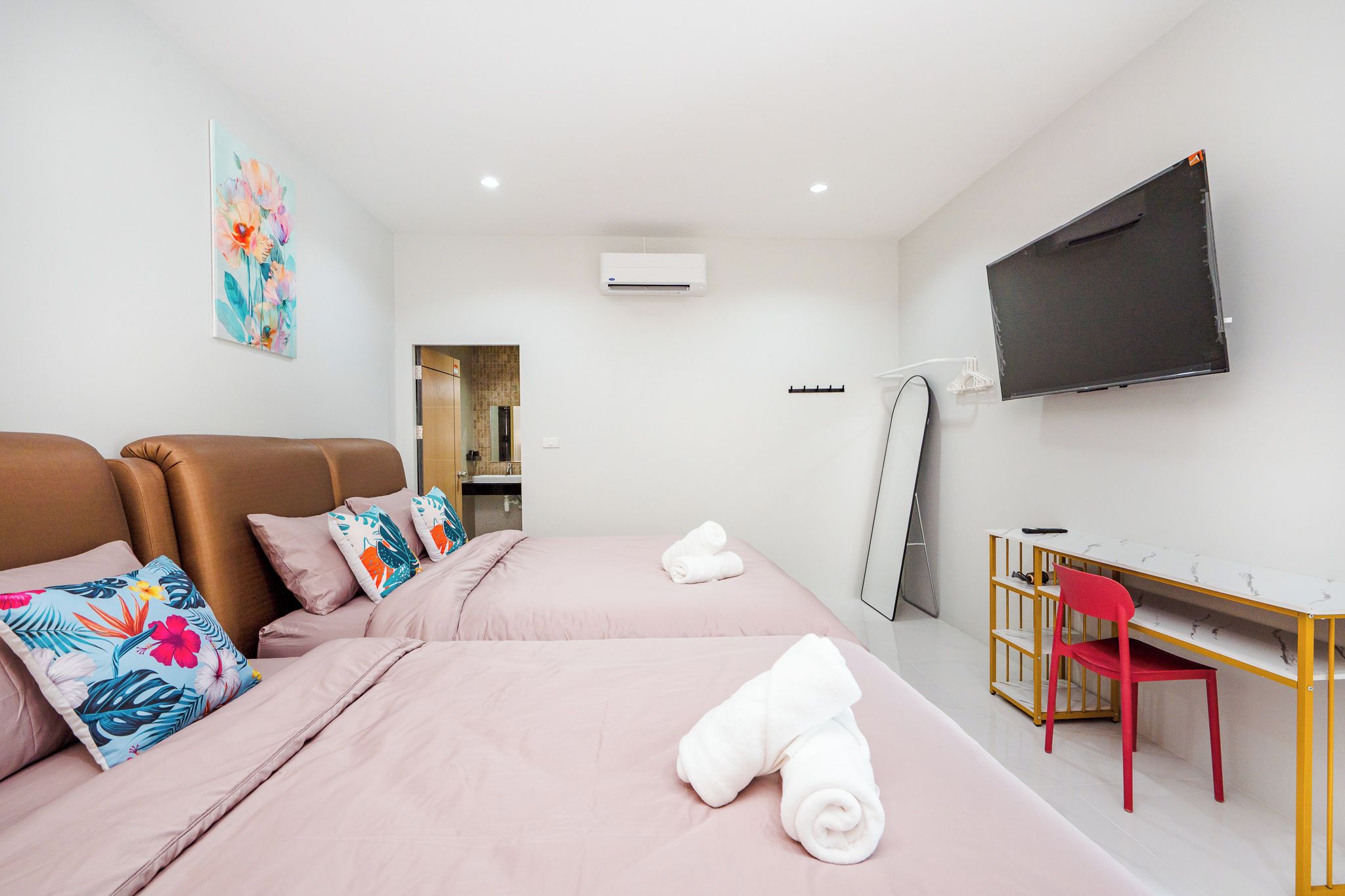 A hotel room with a bed, a desk, a chair, a TV, and an air conditioning unit.