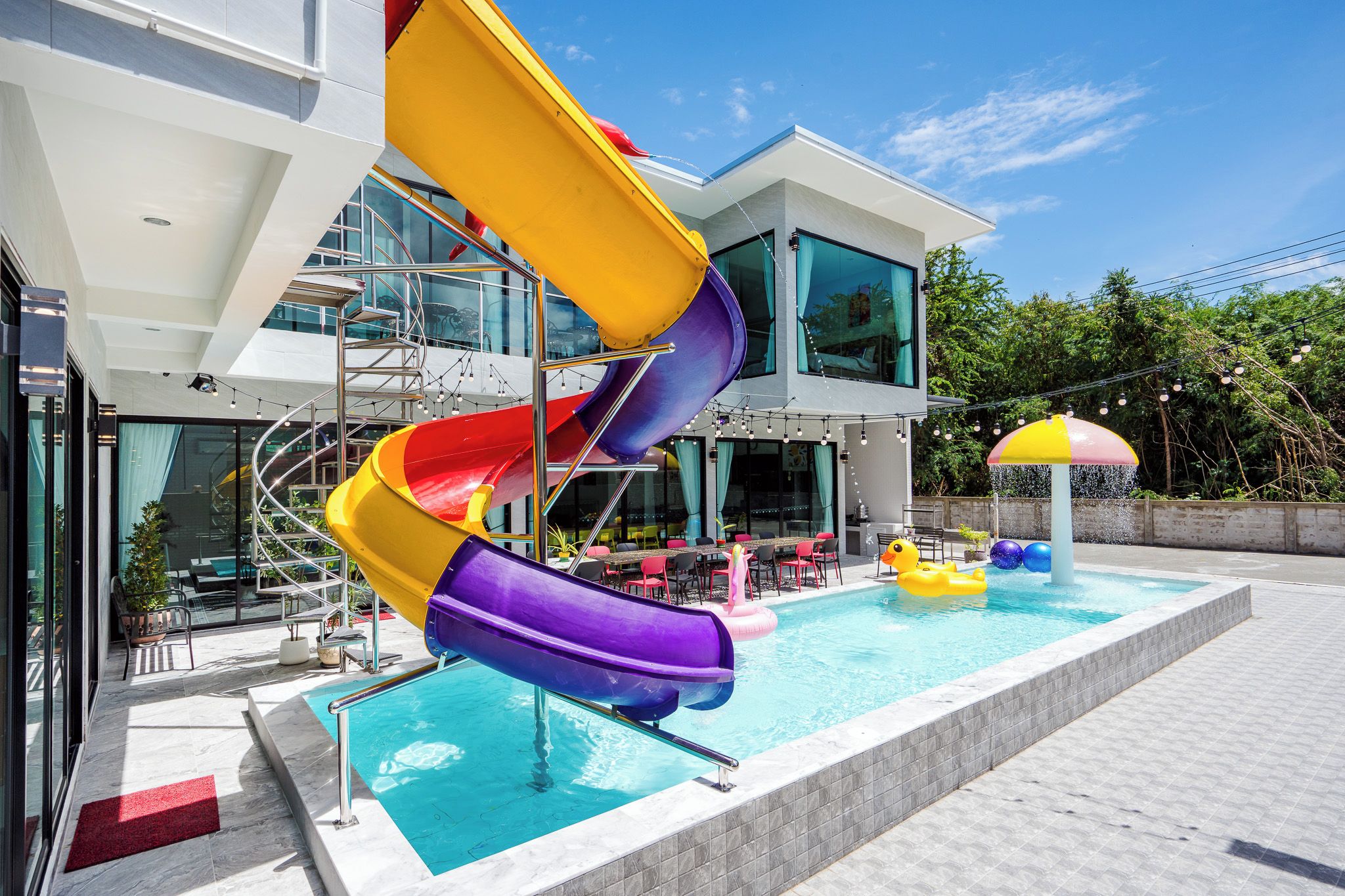 Un edificio moderno con área de piscina, tobogán de varios colores y un pato flotador.