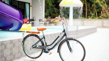 Una bicicleta con una canasta estacionada cerca de una piscina con un paraguas colorido.