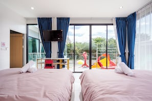 Quarto de hotel com duas camas, uma escrivaninha, televisão e varanda com escorrega.