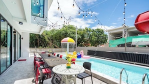 An outdoor pool area with a table and chairs, surrounded by a pool fence, and string lights overhead. - Love U Pool Villa-Hua Hin (Tambon Hua Hin)