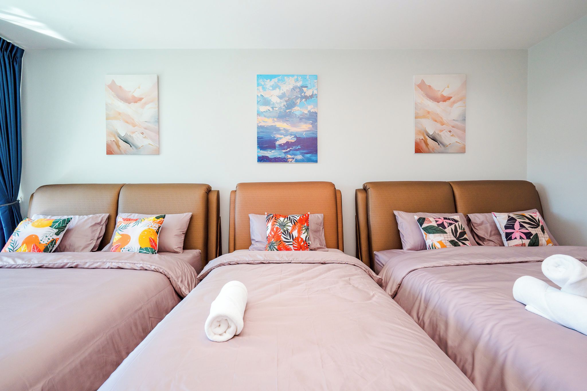 Une chambre d’hôtel avec trois lits, chacun doté d’un oreiller au motif différent, et une vue sur la mer par la fenêtre.