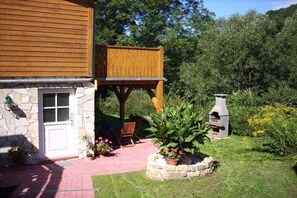 A two-story building with a stone facade, a wooden deck, and a barbecue grill in the yard. - Holiday apartment with 2 bedrooms (Thale\/OT Altenbrak)