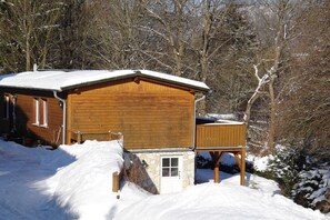 Une cabane en bois avec une entrée en pierre, entourée d’arbres couverts de neige.