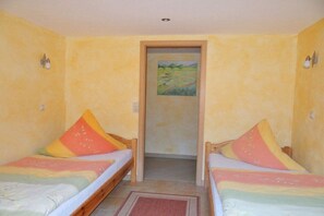 A room with two beds, each with colorful pillows, a door leading to another room, and a painting on the wall. - Holiday apartment with 2 bedrooms (Thale\/OT Altenbrak)