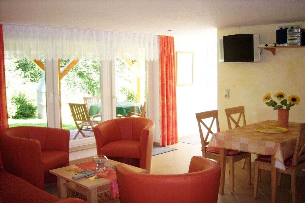 Une pièce comprenant une table à manger, des chaises, un téléviseur fixé au mur et une fenêtre avec des rideaux.