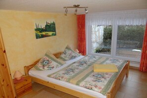 Een slaapkamer met een houten bed, een nachtkastje, een lamp, een schilderij aan de muur en een raam met gordijnen.
