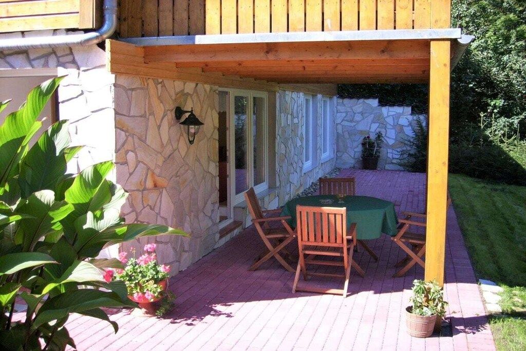 En udendørs terrasse med stenvæg, træmøbler og plantekrukker.